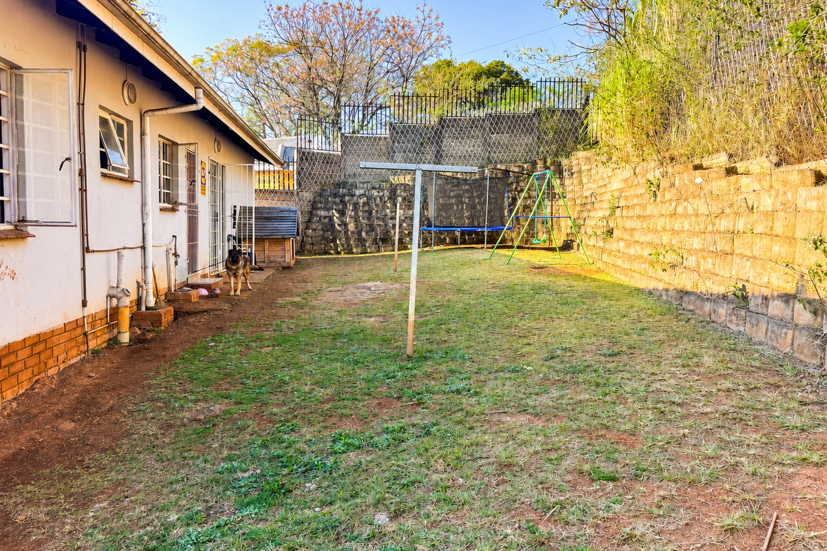 Rear garden area featuring a large stone retaining wall, lawn space, and direct access to the house via security gates.