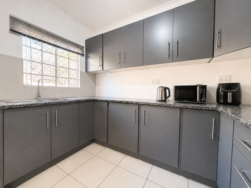 Modern kitchen featuring sleek grey cabinetry, durable laminate countertops, a stainless steel double sink, and tiled flooring with ample storage space.