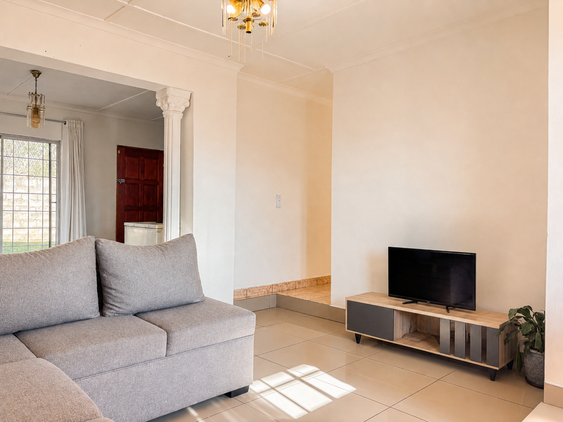 A bright living room featuring tiled flooring, a decorative column, and a sliding glass door providing natural light and access to the exterior.