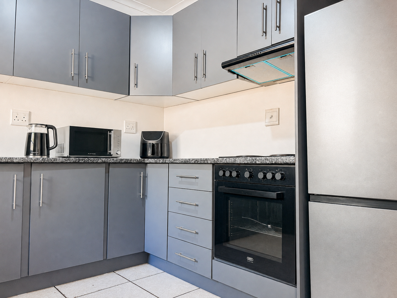 Modern kitchen featuring grey built-in cabinetry, dark laminate countertops, a built-in oven with extractor fan, and tiled flooring.