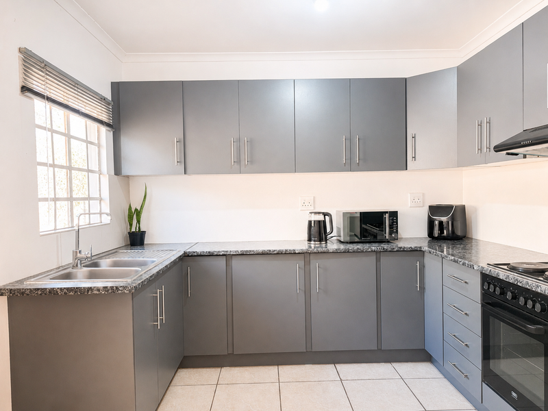 Modern kitchen featuring grey cabinetry, laminate countertops, stainless steel double sink, and integrated oven with hob and extractor fan.