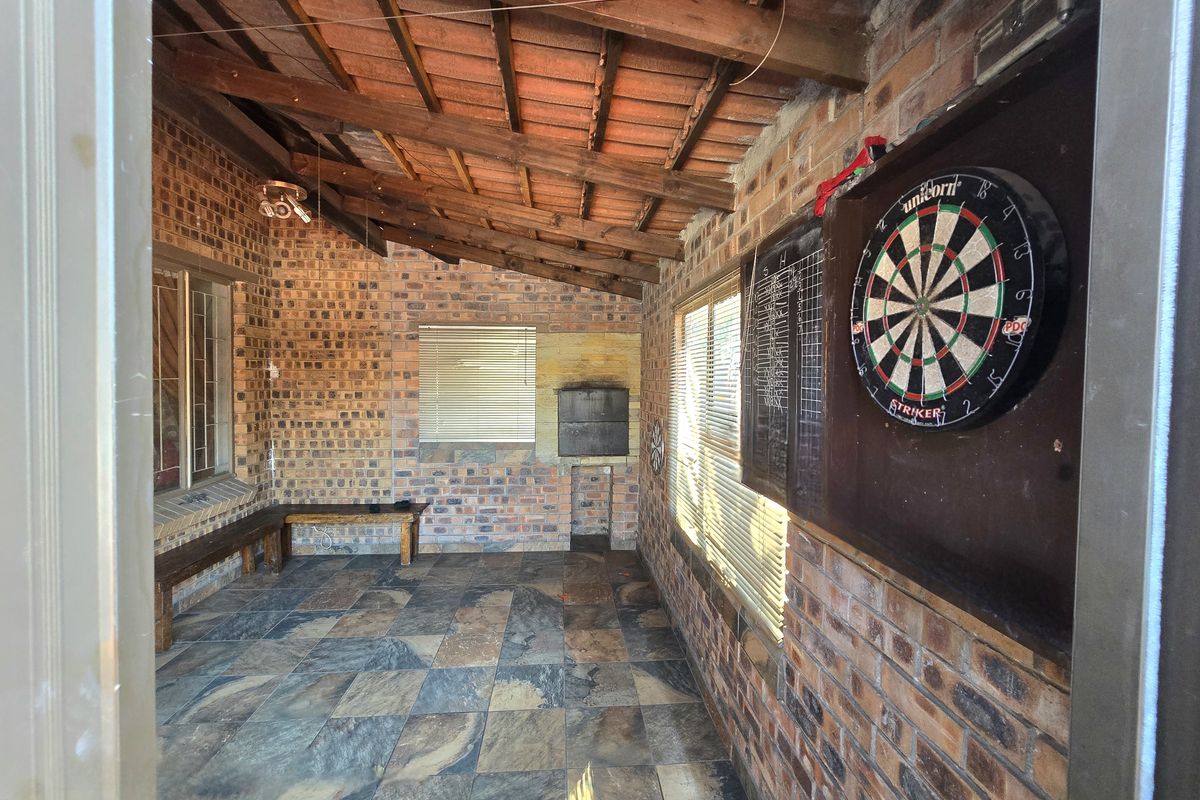 Covered outdoor patio featuring exposed brick walls, timber beam ceiling, tiled flooring, and a built-in braai area, ideal for entertainment.