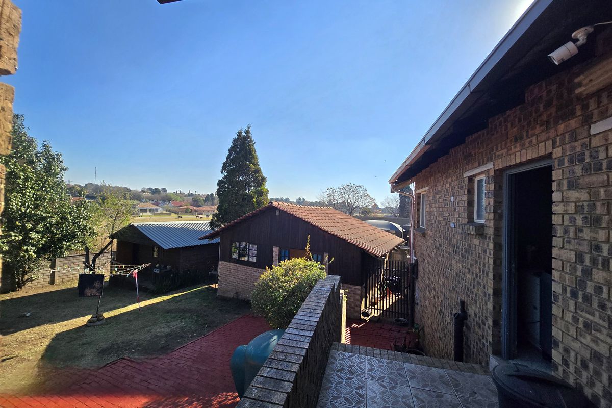 Rear view of the property featuring a brick facade, tiled patio area, and a spacious garden with an outbuilding.