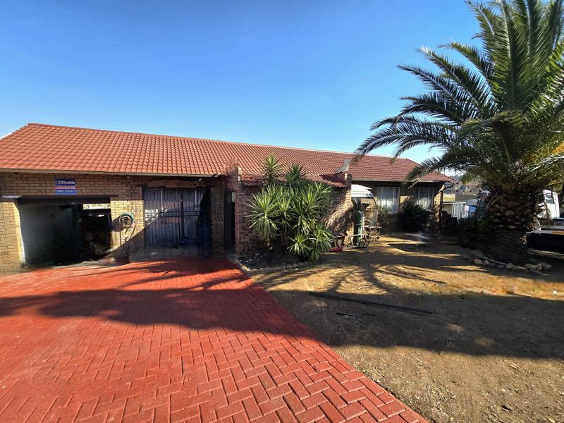 Front elevation of a brick house featuring a red tiled roof, paved driveway, and established garden area.