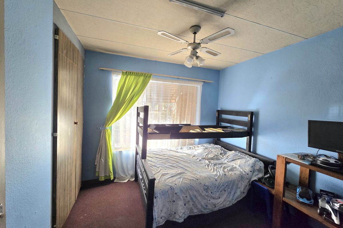 A bedroom featuring a built-in wardrobe, ceiling fan, and carpeted flooring. The room requires cosmetic updates to improve its overall condition and appeal.
