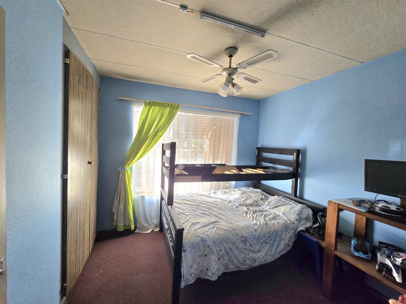 A bedroom featuring a built-in wardrobe, ceiling fan, and carpeted flooring. The room requires cosmetic updates to improve its overall condition and appeal.