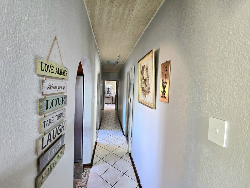 A narrow residential hallway featuring tiled flooring and an arched entryway, showing signs of wear on the ceiling.