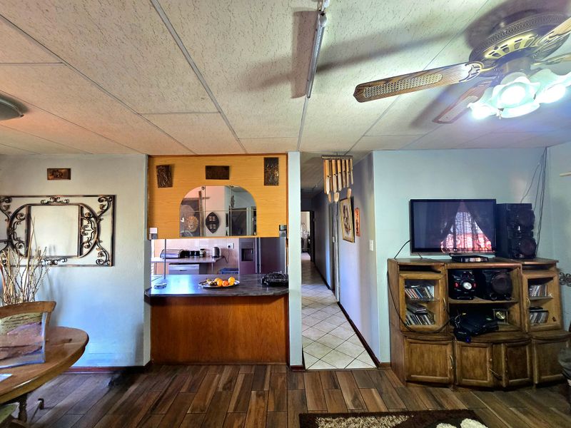 Open plan living area featuring laminate flooring, a pass-through window to the kitchen, and a ceiling fan, connecting to a tiled hallway.