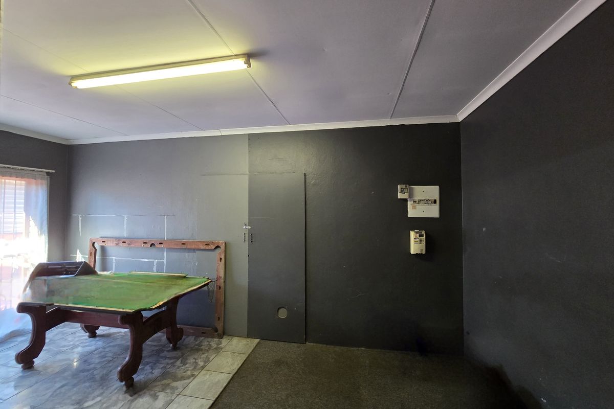 A multi-purpose living area featuring tiled flooring, a fluorescent light fixture, and an exposed electrical distribution board on a dark-painted wall.