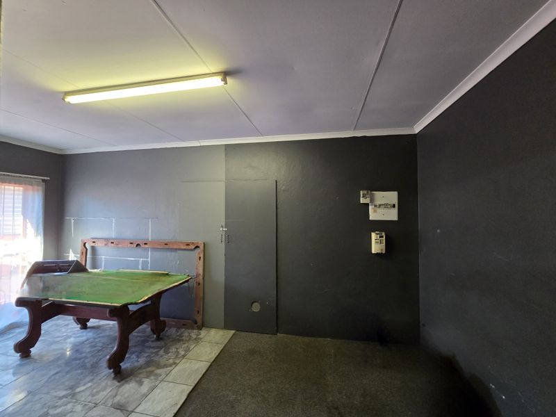 A multi-purpose living area featuring tiled flooring, a fluorescent light fixture, and an exposed electrical distribution board on a dark-painted wall.