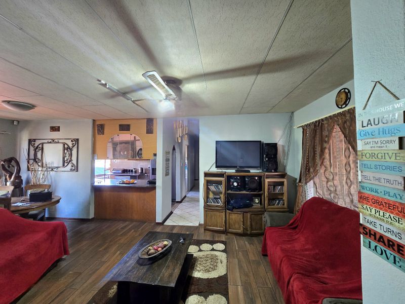 Open plan living area featuring laminate flooring, a breakfast bar connecting to the kitchen, and a tiled hallway leading to other rooms.