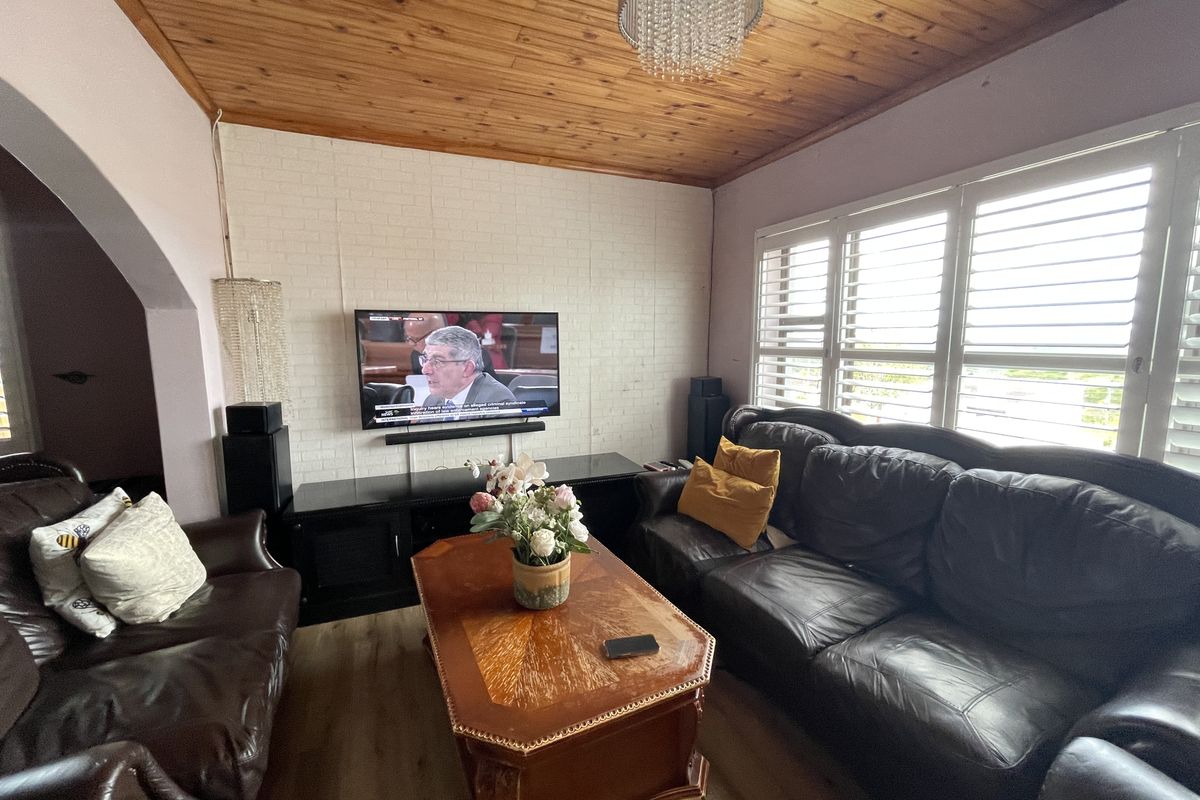 A cozy living room featuring a timber-clad ceiling, a white brick feature wall, and plantation shutters that allow for natural light.
