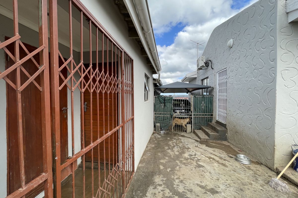 A side passage or rear exterior area featuring concrete paving, security gates, and textured wall finishes.