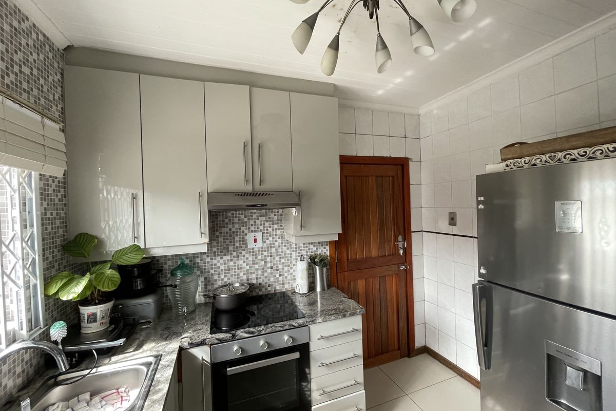 A functional kitchen featuring built-in cabinetry, granite countertops, an electric hob with extractor, and tiled finishes throughout.