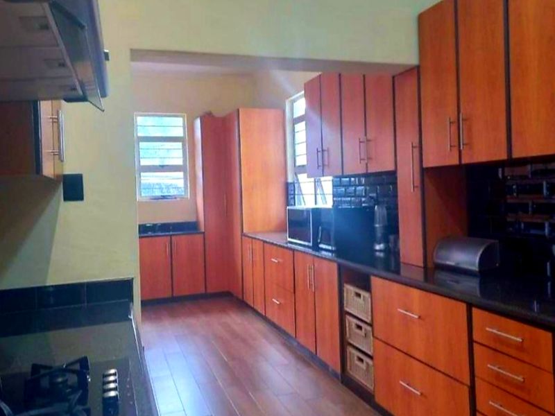 A functional kitchen featuring wood-finish cabinetry, dark countertops, a gas hob with extractor fan, and tiled backsplash with laminate flooring.