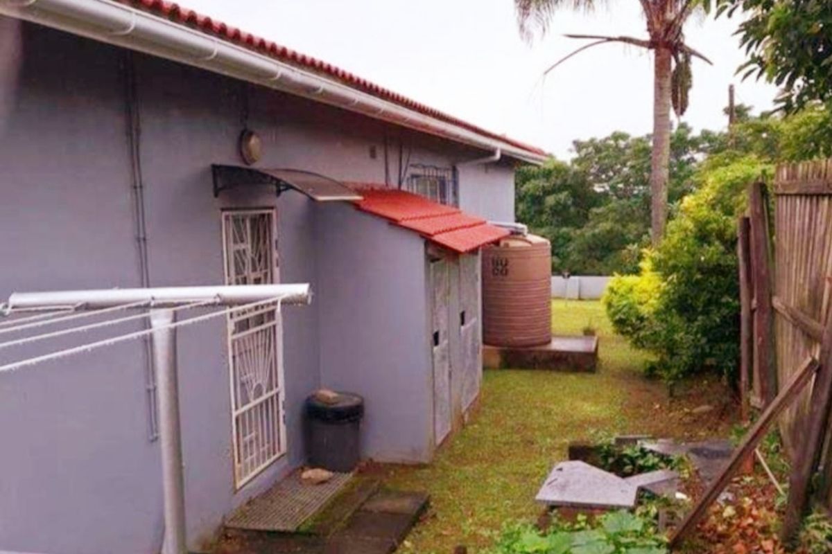Rear exterior view of the property featuring a water storage tank, guttering system, and a small paved area with security gate access.