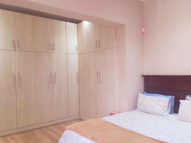 A bedroom featuring extensive light wood-toned built-in wardrobes and laminate flooring, providing ample storage space.