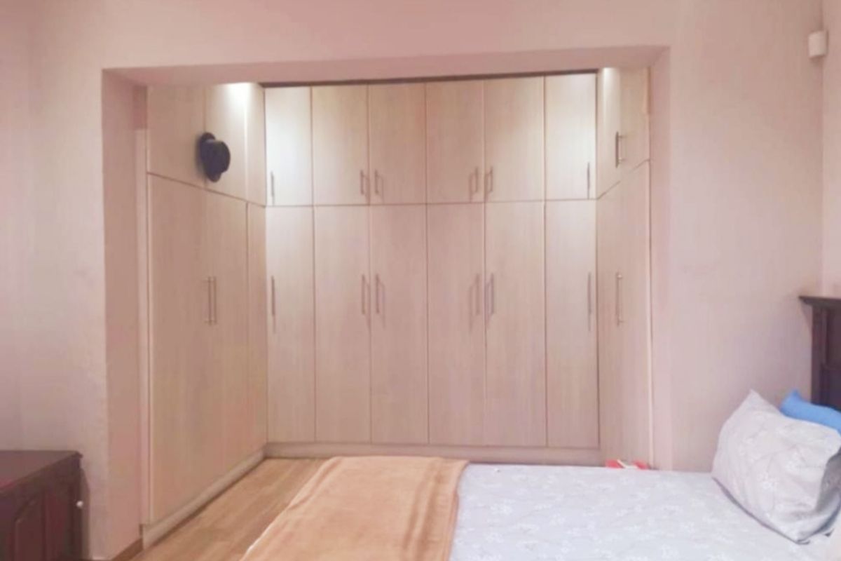 A bedroom featuring extensive light wood built-in cupboards providing ample storage space, complemented by laminate flooring and recessed lighting.