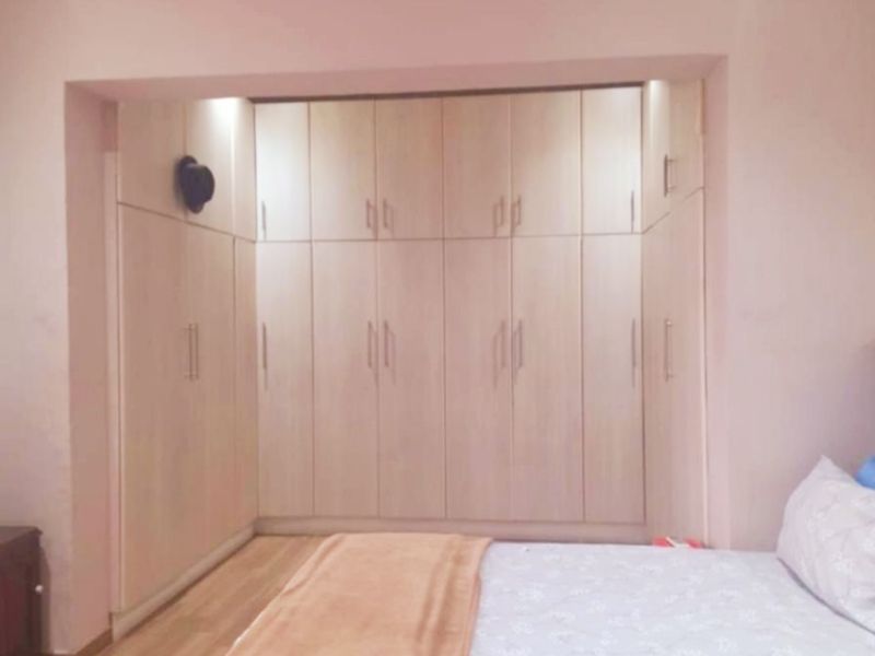 A bedroom featuring extensive light wood built-in cupboards providing ample storage space, complemented by laminate flooring and recessed lighting.