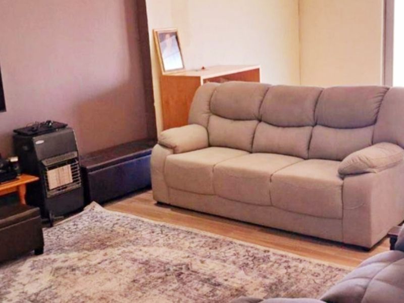 A living room area featuring laminate flooring and a neutral wall finish, providing a functional space for relaxation.