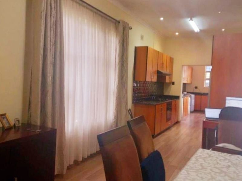 Open-plan living and kitchen area featuring laminate flooring, wooden cabinetry, and integrated appliances, with a view through to a secondary kitchen or scullery area.