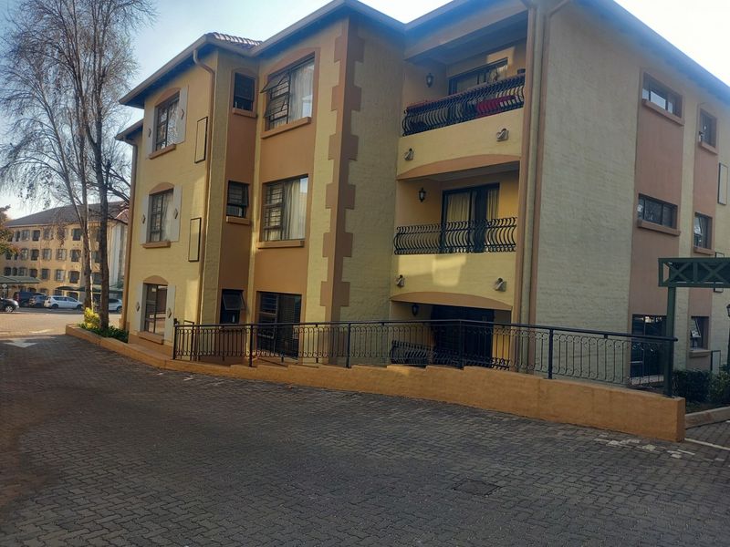 Exterior view of a multi-story apartment complex featuring paved driveway access, wrought iron balcony railings, and established exterior wall finishes.