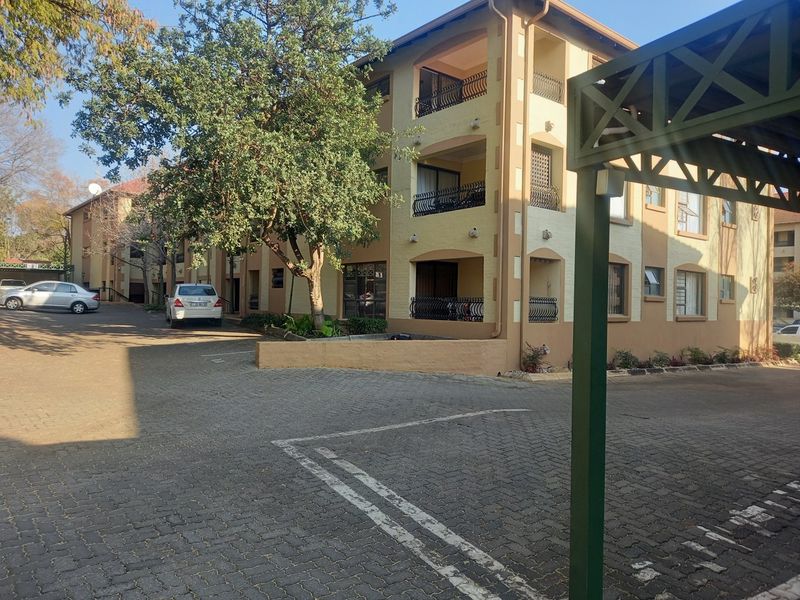 Exterior view of a multi-story apartment complex featuring paved parking areas, covered carports, and private balconies with wrought iron railings.