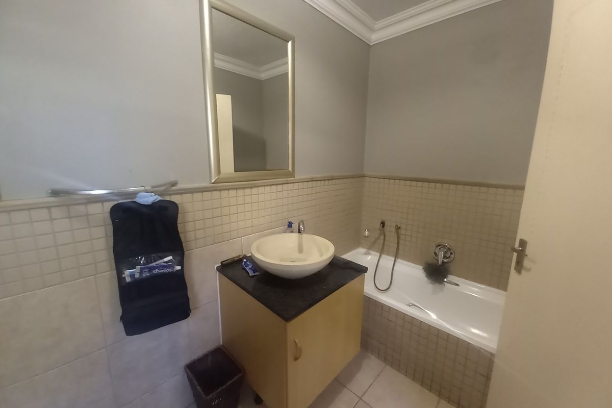 A functional bathroom featuring a vessel sink vanity, a bathtub with wall-mounted fixtures, and neutral tiled wall accents.