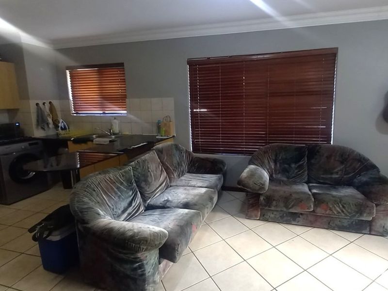 Open plan living area featuring tiled flooring, kitchen cabinetry with integrated sink, and large windows with venetian blinds.