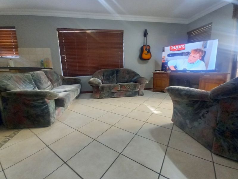 A living room featuring tiled flooring, crown molding, and venetian blinds, providing a functional space for relaxation.