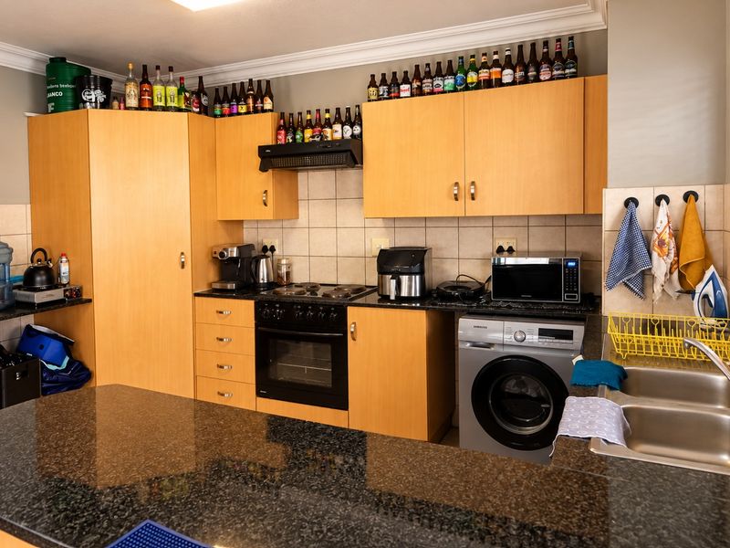 Functional kitchen featuring granite countertops, laminate cabinetry, built-in oven, electric hob, and integrated laundry space with a double bowl stainless steel sink.