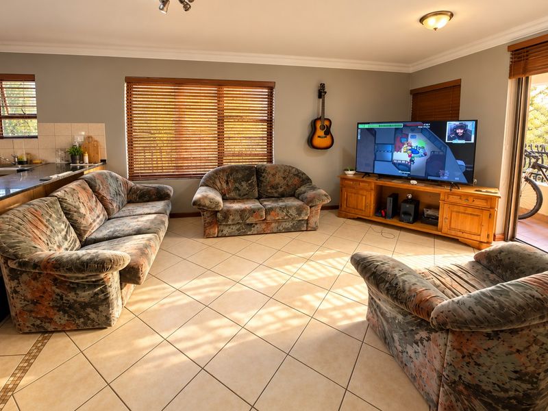 An open-plan living area featuring tiled flooring, wooden blinds, and direct access to an outdoor patio through a sliding door.