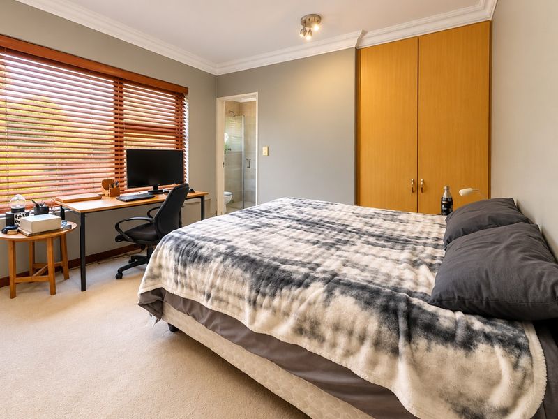A well-maintained bedroom featuring built-in wardrobes, carpet flooring, timber blinds, and an attached en-suite bathroom.