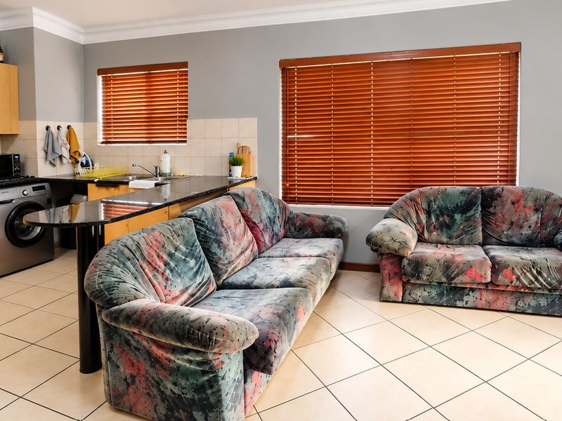 Open plan kitchen and living area featuring tiled flooring, granite countertops, built-in cabinetry, and large windows with venetian blinds.