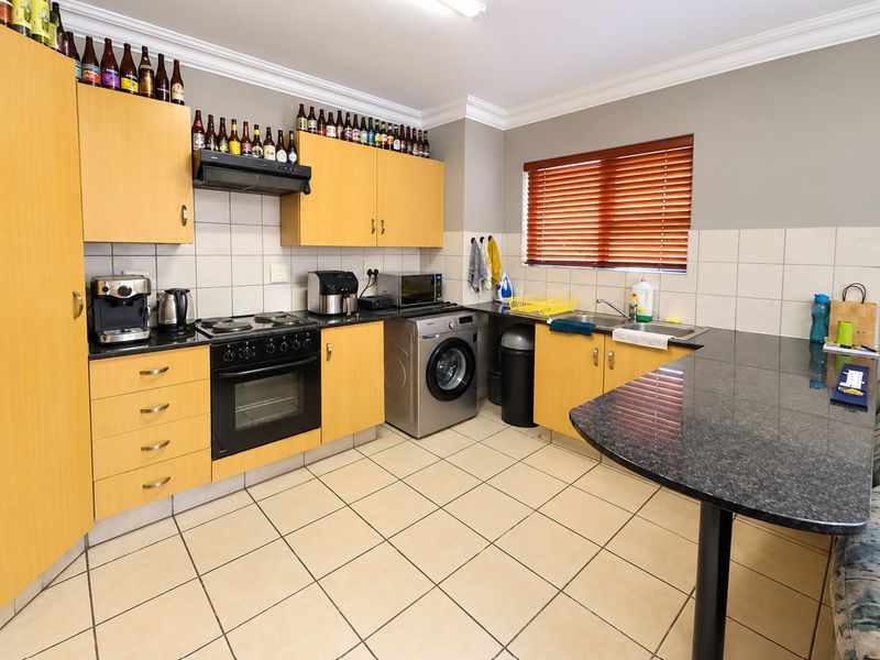 A functional kitchen featuring light wood cabinetry, dark granite countertops, tiled flooring, and integrated appliances including an oven, hob, and extractor fan.