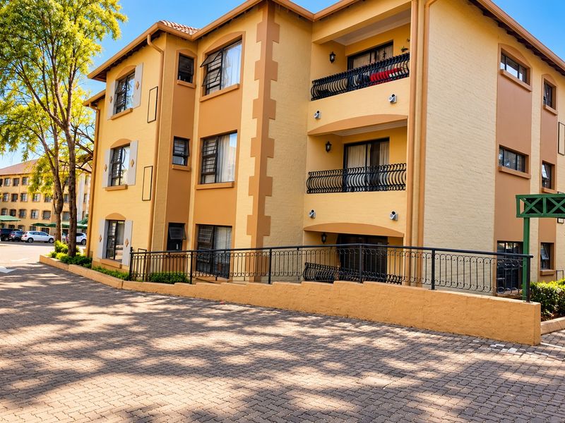 A view of the apartment building exterior featuring a paved driveway, multiple levels with balconies, and wrought iron railings.