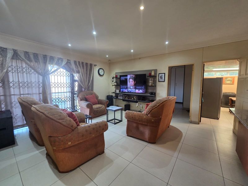 A well-lit living room featuring tiled flooring, recessed downlights, and a built-in media unit, with direct access to an outdoor area via a security gate.
