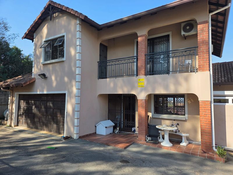Two-story residential facade featuring a tiled roof, balcony with wrought iron railings, brick pillar accents, and an integrated garage.