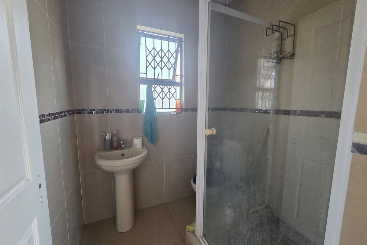 A functional bathroom featuring a pedestal basin, tiled finishes, and a glass-enclosed shower with security bars on the window.