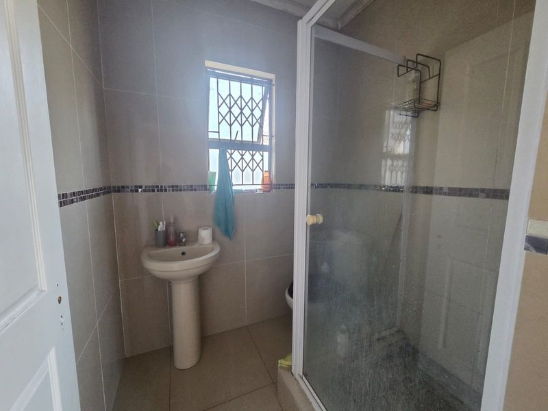 A functional bathroom featuring a pedestal basin, tiled finishes, and a glass-enclosed shower with security bars on the window.