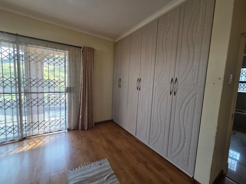 A spacious bedroom featuring light wood-grain built-in cupboards, laminate flooring, and a sliding door providing access to the exterior.