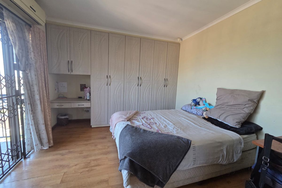 A bedroom featuring built-in cupboards with an integrated desk, laminate flooring, and a sliding door leading to an outdoor area with a security gate.
