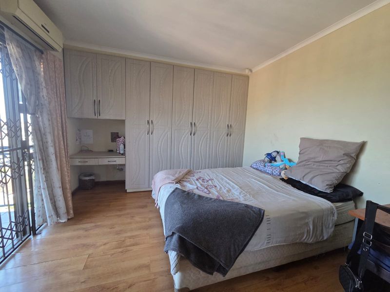 A bedroom featuring built-in cupboards with an integrated desk, laminate flooring, and a sliding door leading to an outdoor area with a security gate.