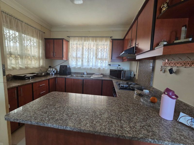 A functional kitchen featuring granite countertops, ample wooden cabinetry, a built-in gas hob with extractor fan, and a double basin sink.