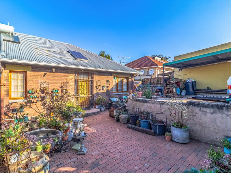 Rear exterior view featuring a brick facade, corrugated metal roof with solar installations, and a paved patio area with a low retaining wall.