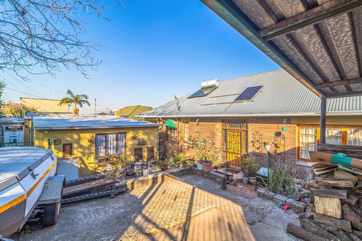 Rear exterior view of a brick house featuring a corrugated metal roof, solar water heating system, and a concrete patio area.