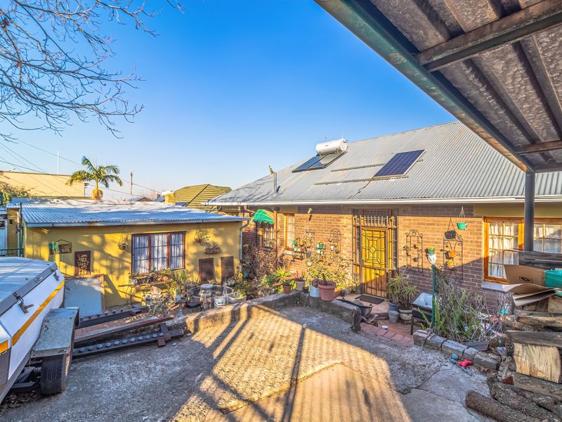 Rear exterior view of a brick house featuring a corrugated metal roof, solar water heating system, and a concrete patio area.