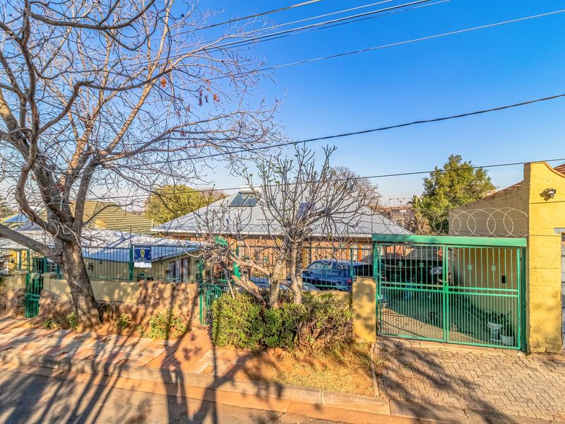 Front exterior view of the property featuring a paved driveway, metal security gate with razor wire, and a metal roof with a solar geyser.
