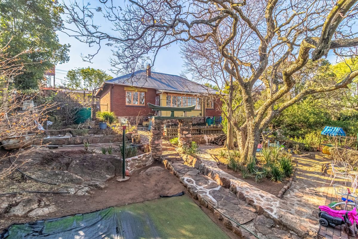 Rear view of a brick house featuring a stone pathway, decorative stone archway, and established garden with mature trees.