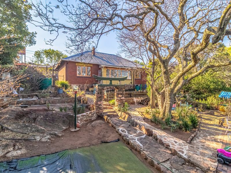 Rear view of a brick house featuring a stone pathway, decorative stone archway, and established garden with mature trees.